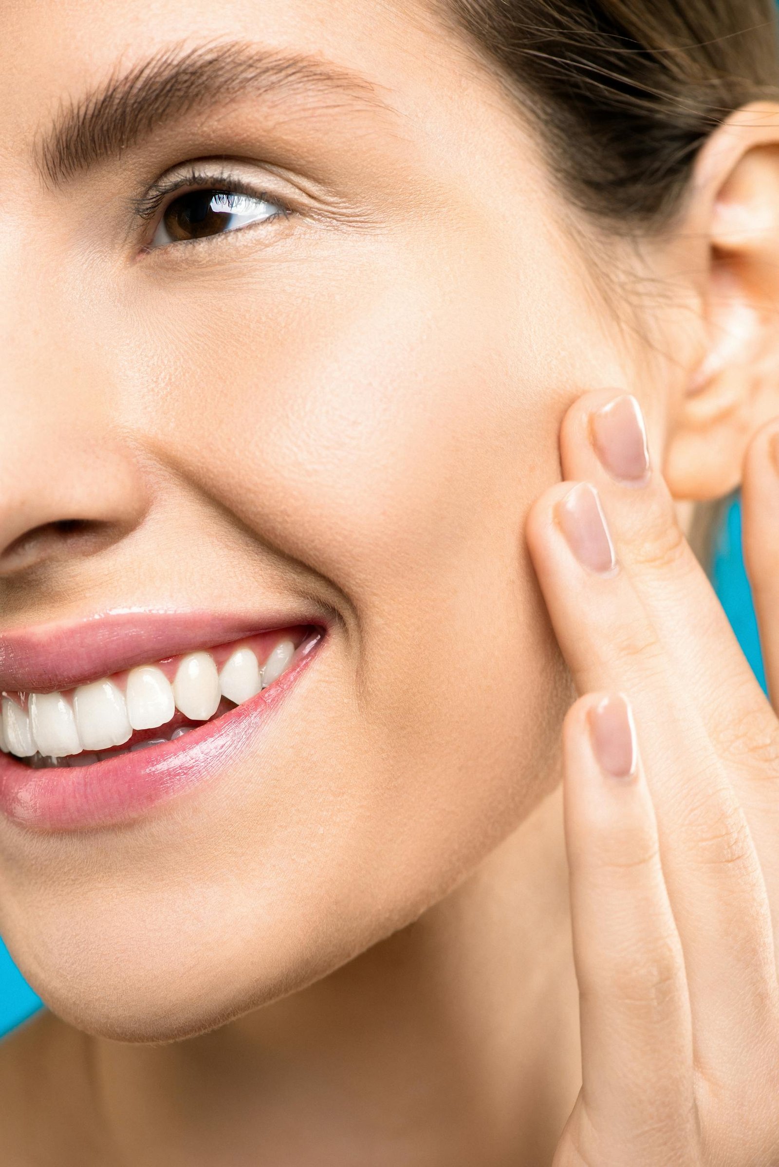A close-up portrait showing a woman gently touching her cheek, showcasing healthy skin and a vibrant smile due to great dermatology service