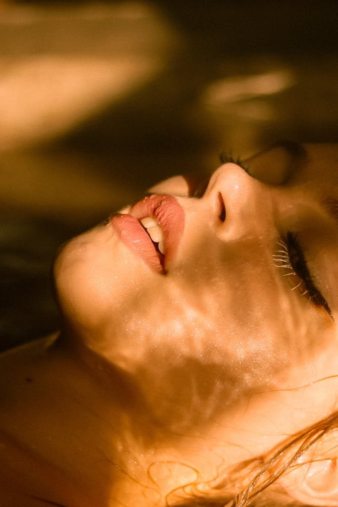 Close-up of a woman's face with sunlight casting shadows, highlighting lips and peaceful expression.
